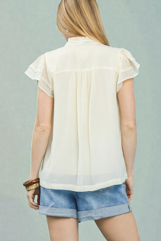 Woman wearing a light-colored blouse and denim shorts against a gray background