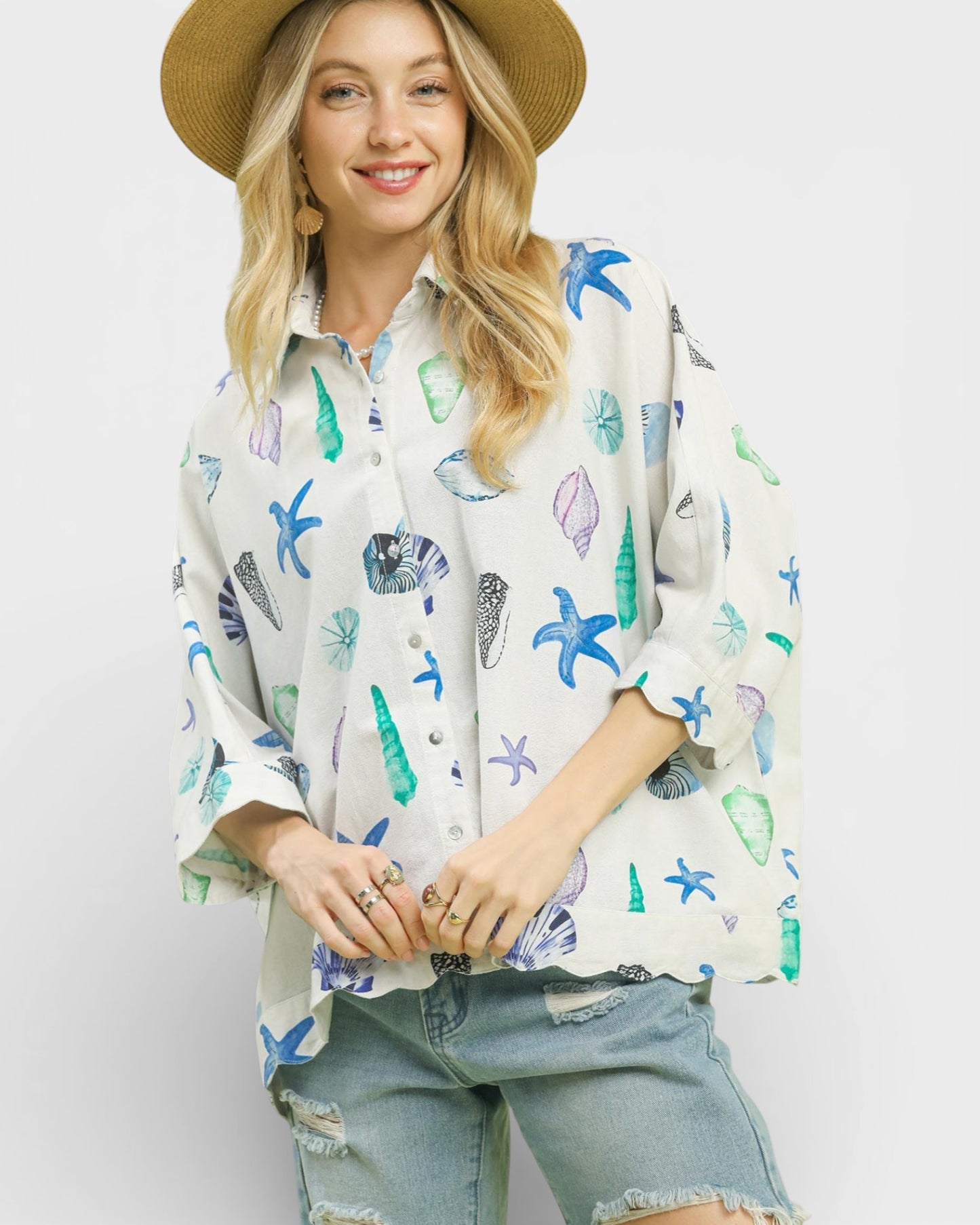 Woman wearing a patterned shirt with starfish design and denim shorts on a white background