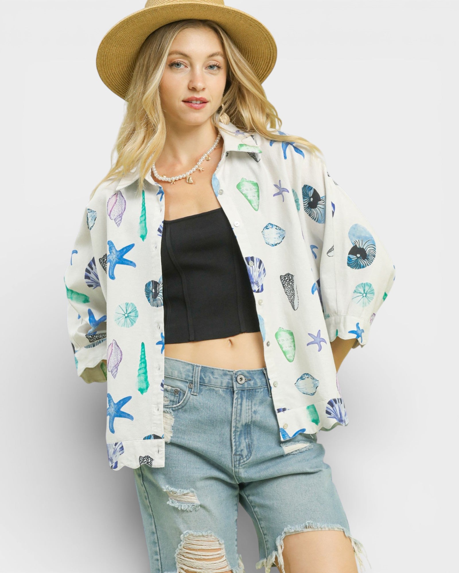 Woman wearing a patterned shirt, black top, and denim shorts against a white background