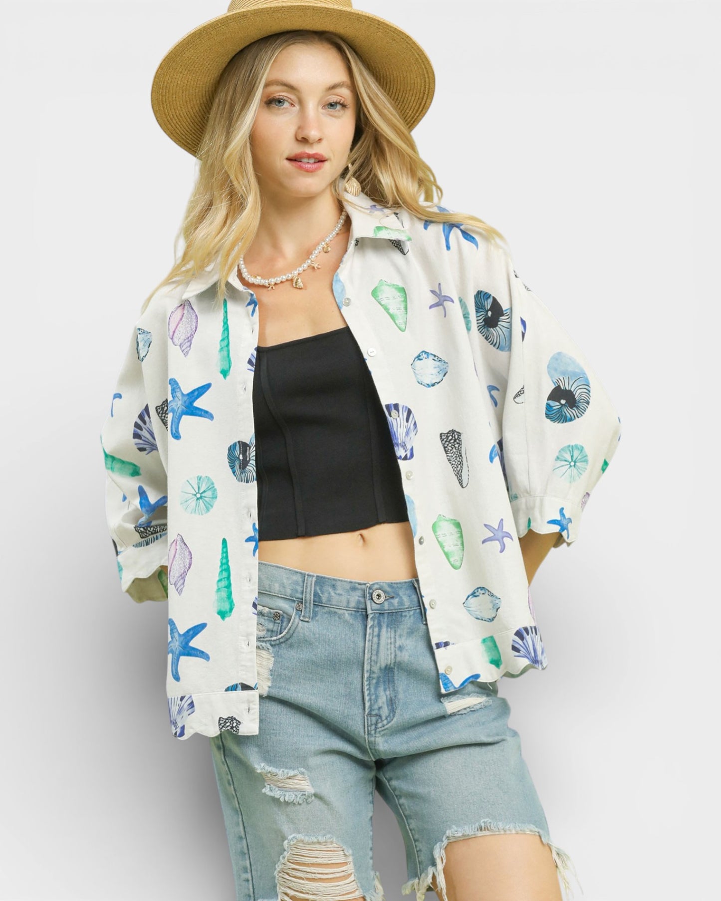 Woman wearing a patterned shirt, black top, and denim shorts against a white background