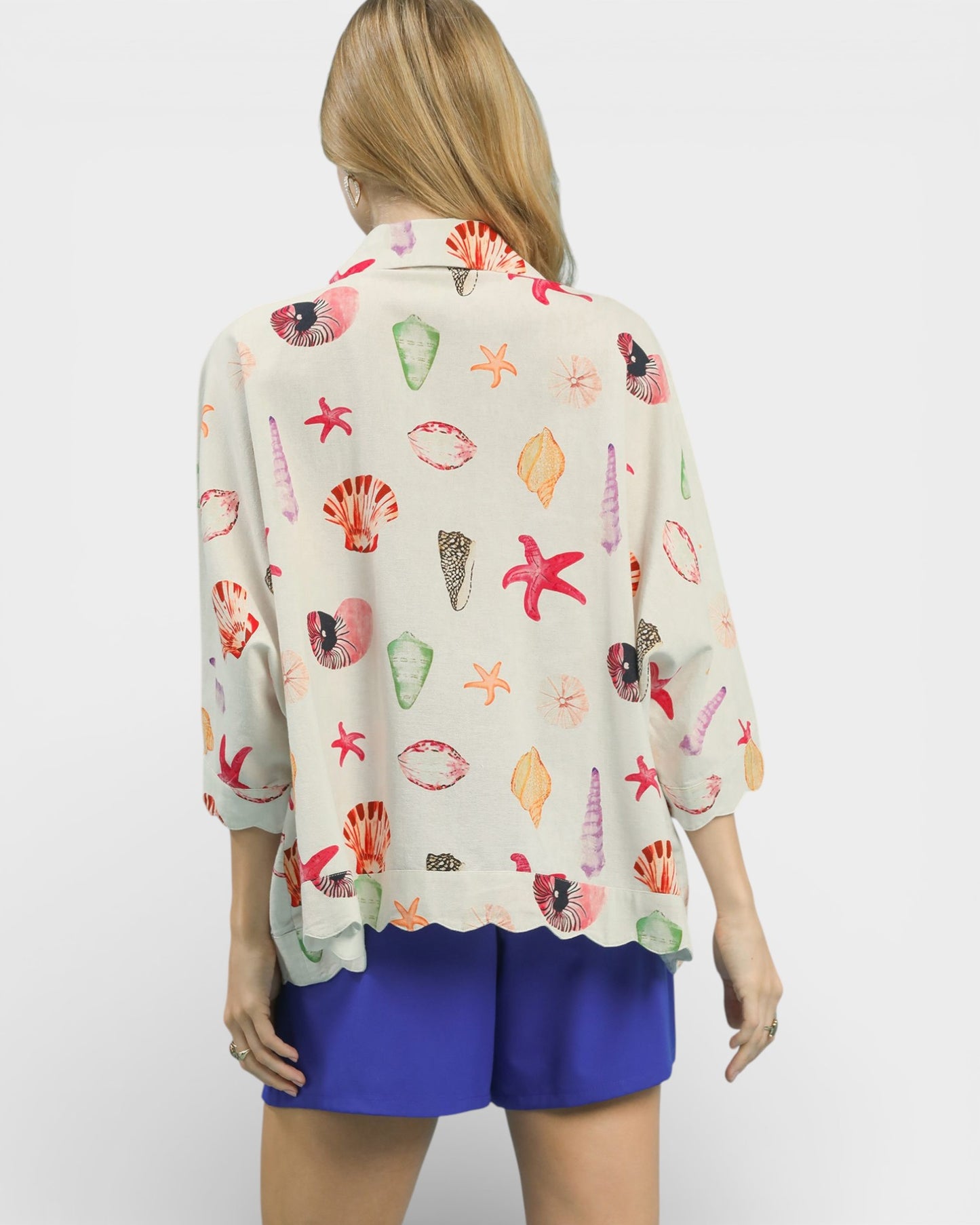 Woman wearing a colorful shell-patterned blouse with blue shorts on a white background