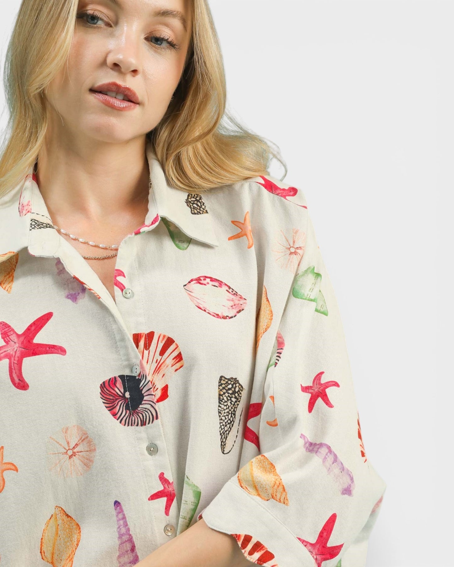Woman wearing a colorful shell patterned shirt on a plain background
