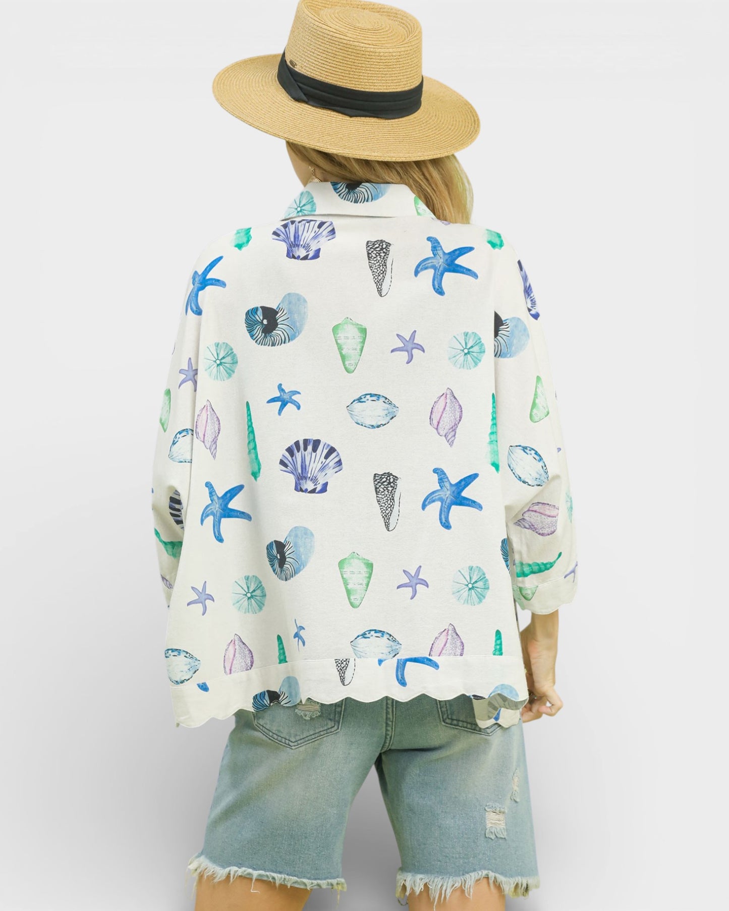 Person wearing a colorful shell-patterned shirt and denim shorts on a white background