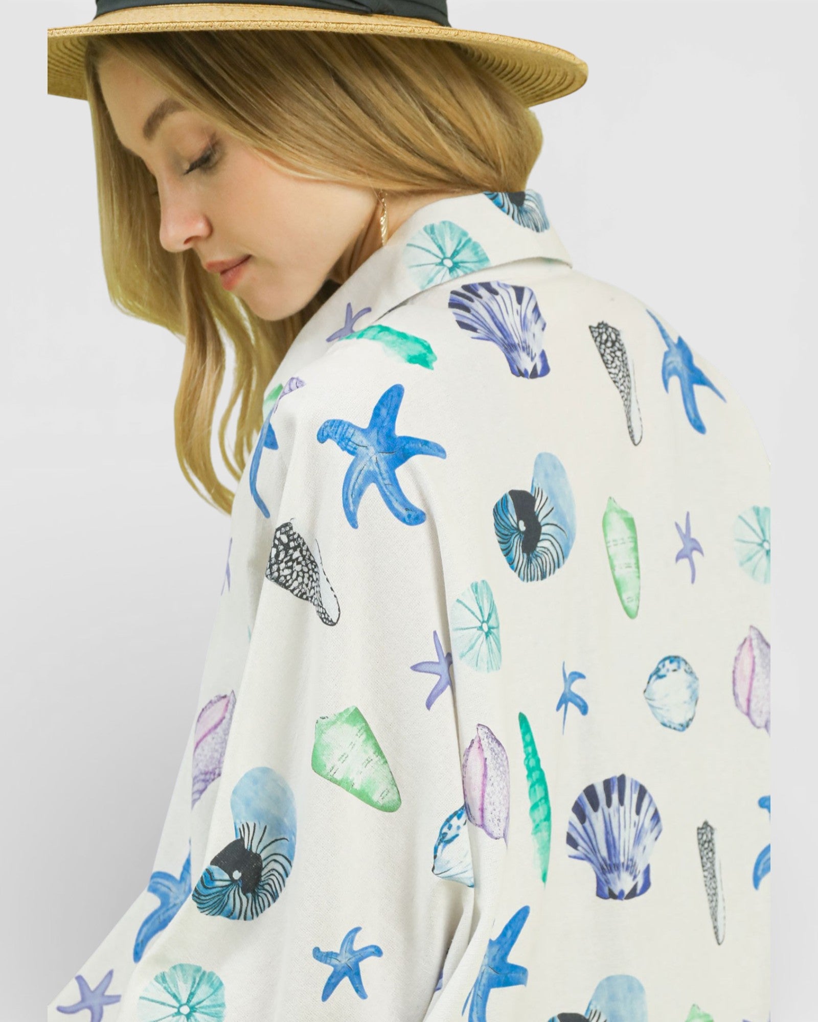 Person wearing a white shirt with colorful shell and starfish patterns on a plain background