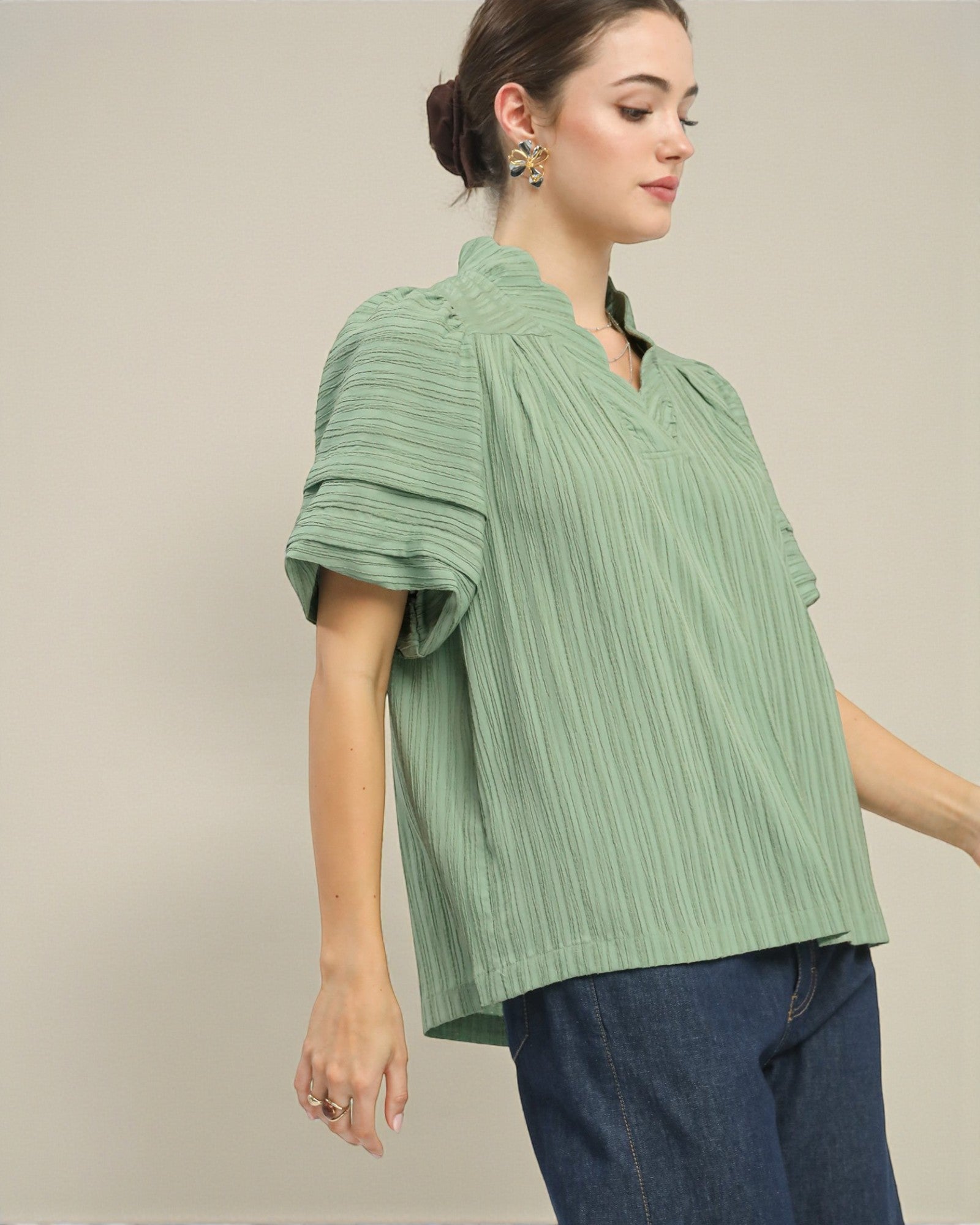 Woman wearing a green pleated blouse and blue jeans against a neutral background