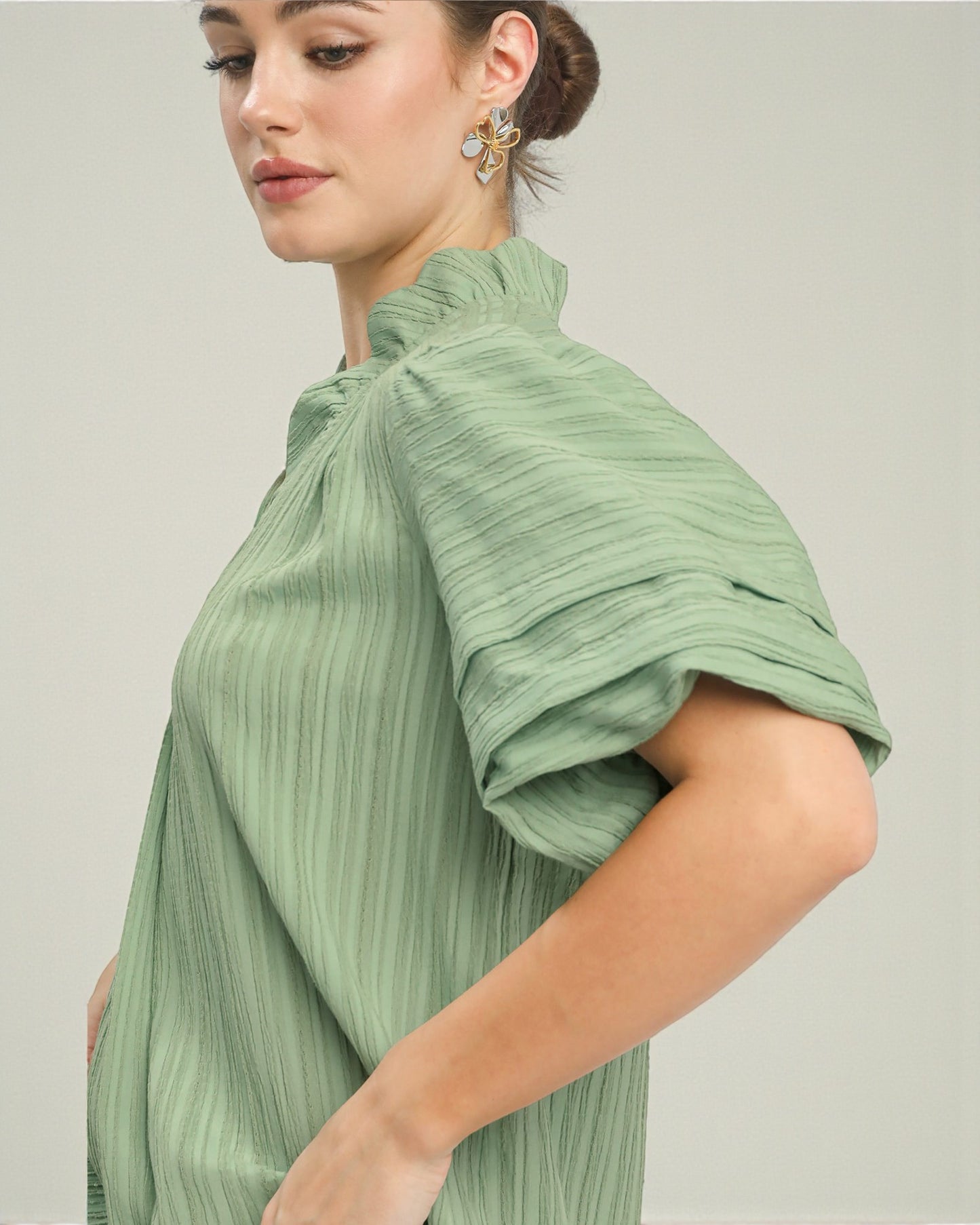 Woman wearing a green pleated top against a plain background