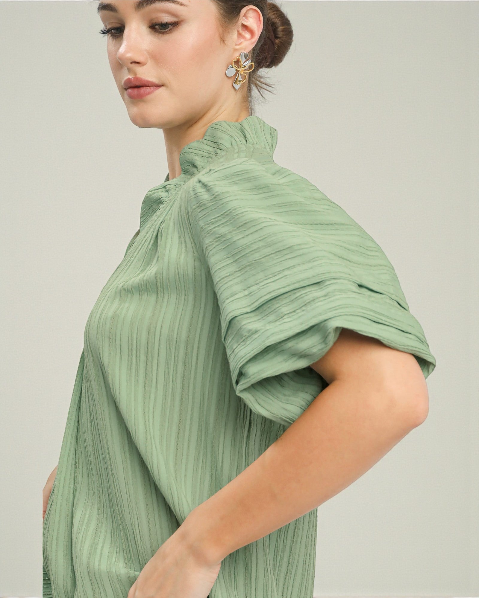Woman wearing a green pleated top against a plain background