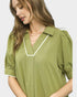 Woman wearing a green blouse with white trim on a light gray background
