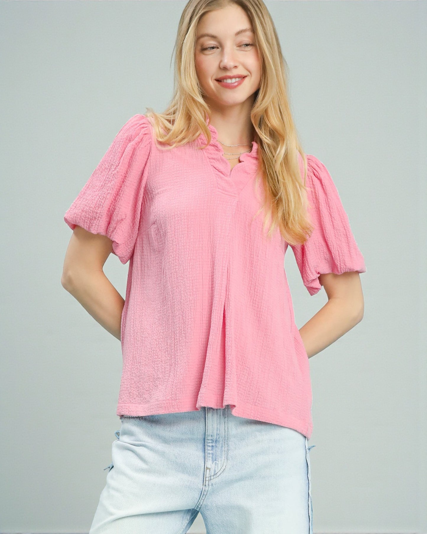 Woman wearing a pink blouse with ruffled sleeves on a gray background
