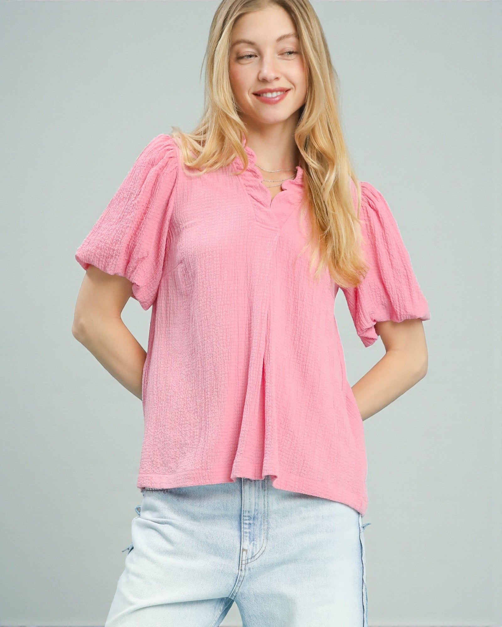 Woman wearing a pink blouse with ruffled sleeves on a gray background