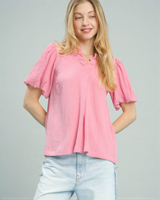 Woman wearing a pink blouse with ruffled sleeves on a gray background