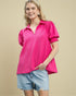 Woman wearing a bright pink blouse and denim shorts on a beige background