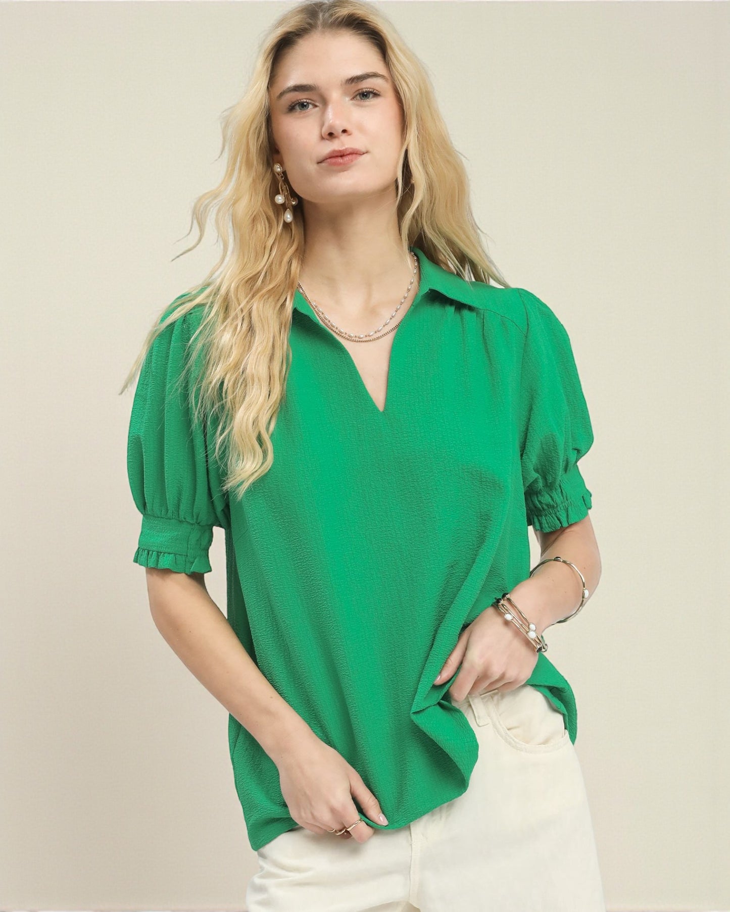 Woman wearing a green blouse with puff sleeves on a beige background