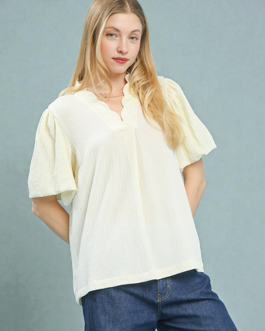 Woman wearing a light-colored blouse and blue jeans against a gray background