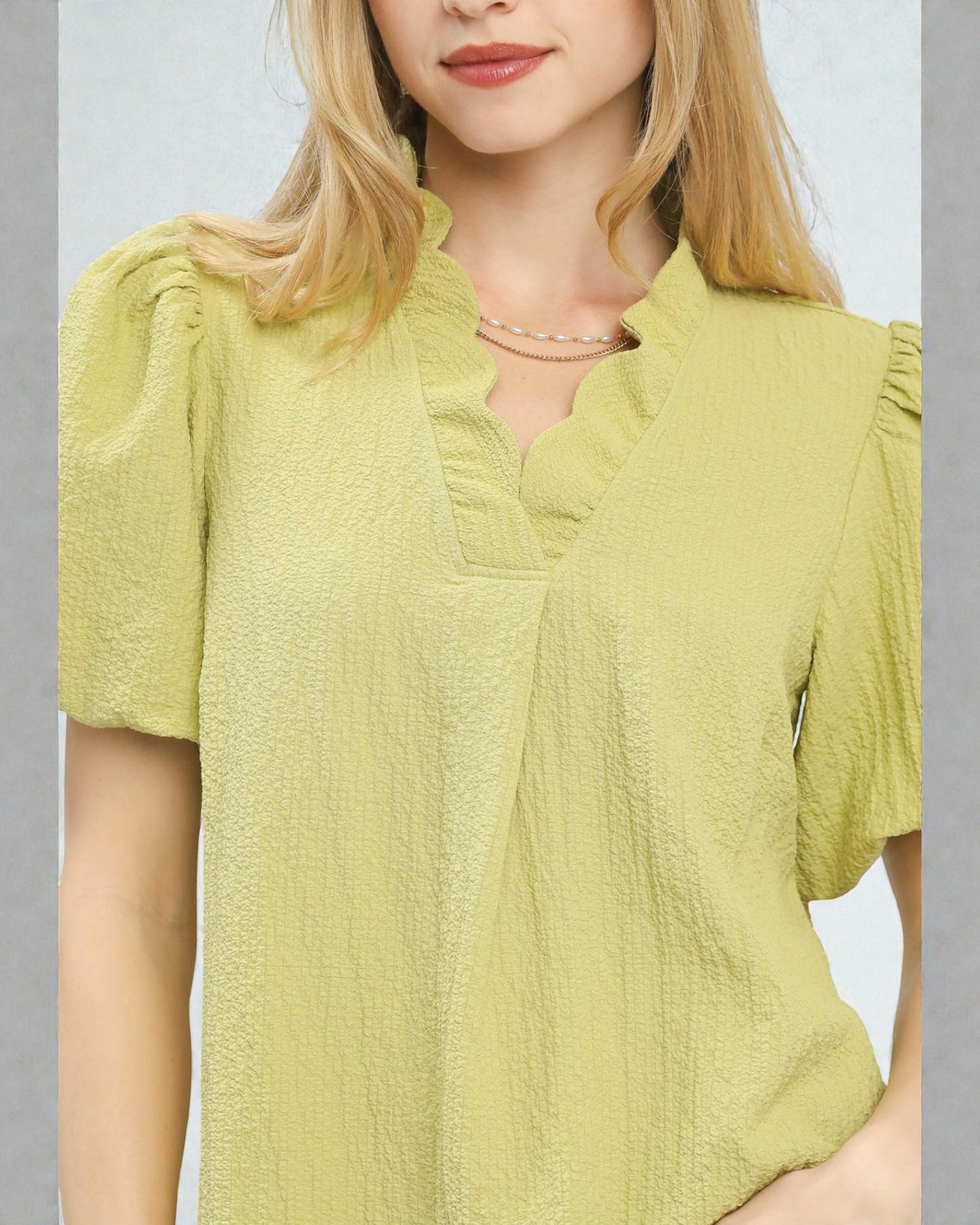 Woman wearing a light green blouse with puff sleeves against a neutral background