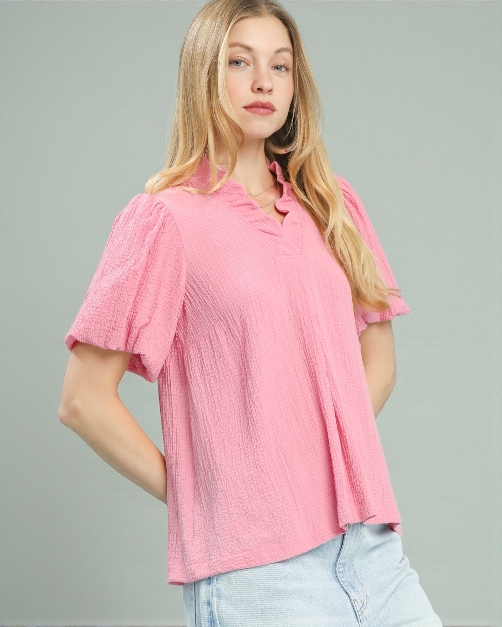 Woman wearing a pink blouse with ruffled sleeves on a gray background