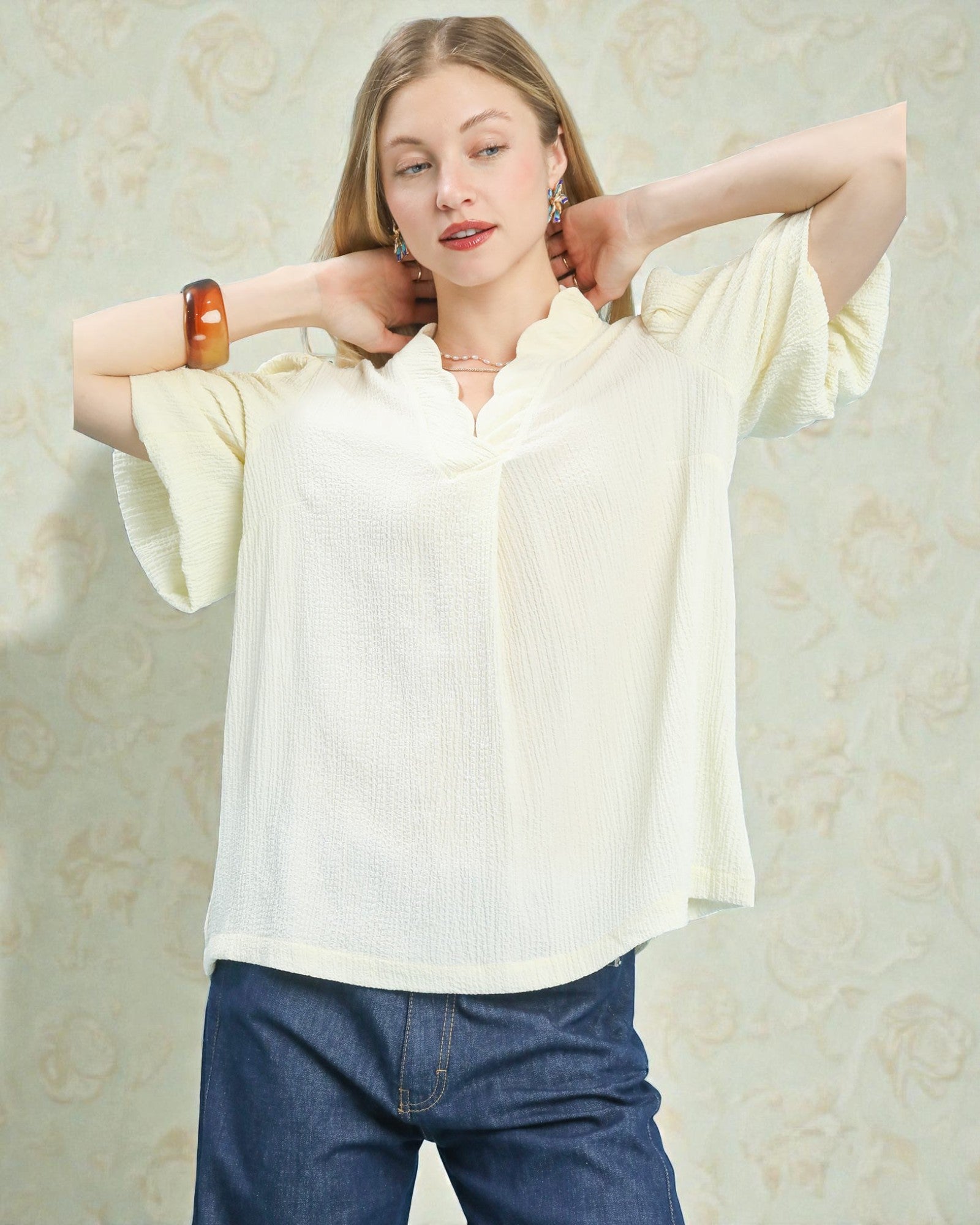 Woman wearing a light-colored blouse and blue jeans against a floral-patterned background