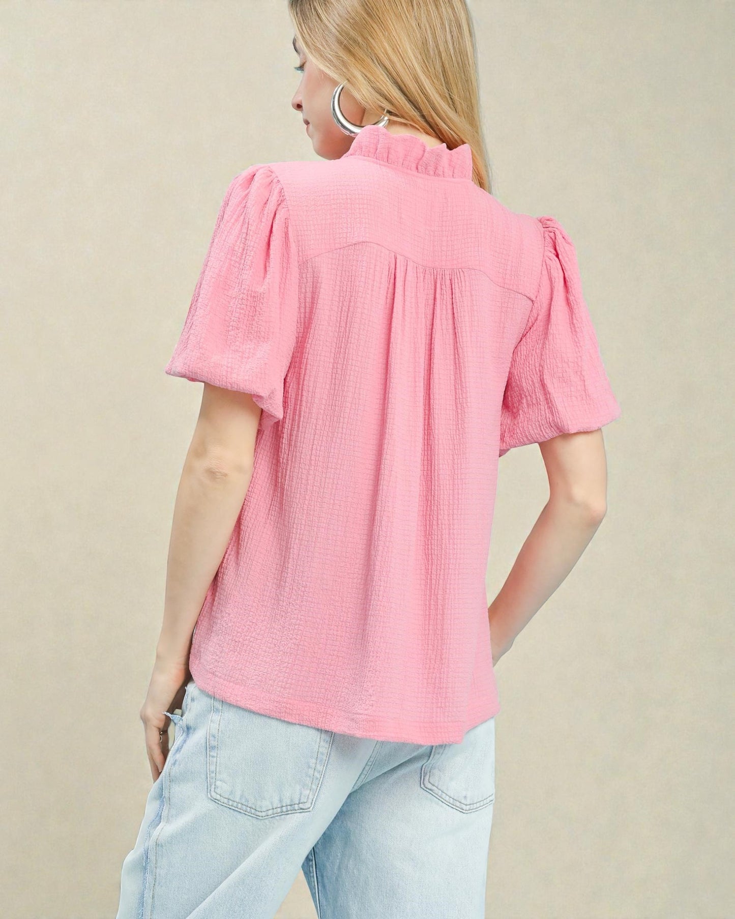 Woman wearing a pink blouse with short sleeves and light blue jeans on a beige background