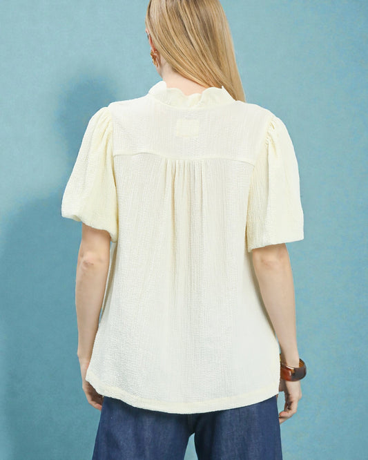 Person wearing a light yellow blouse with short sleeves against a blue background