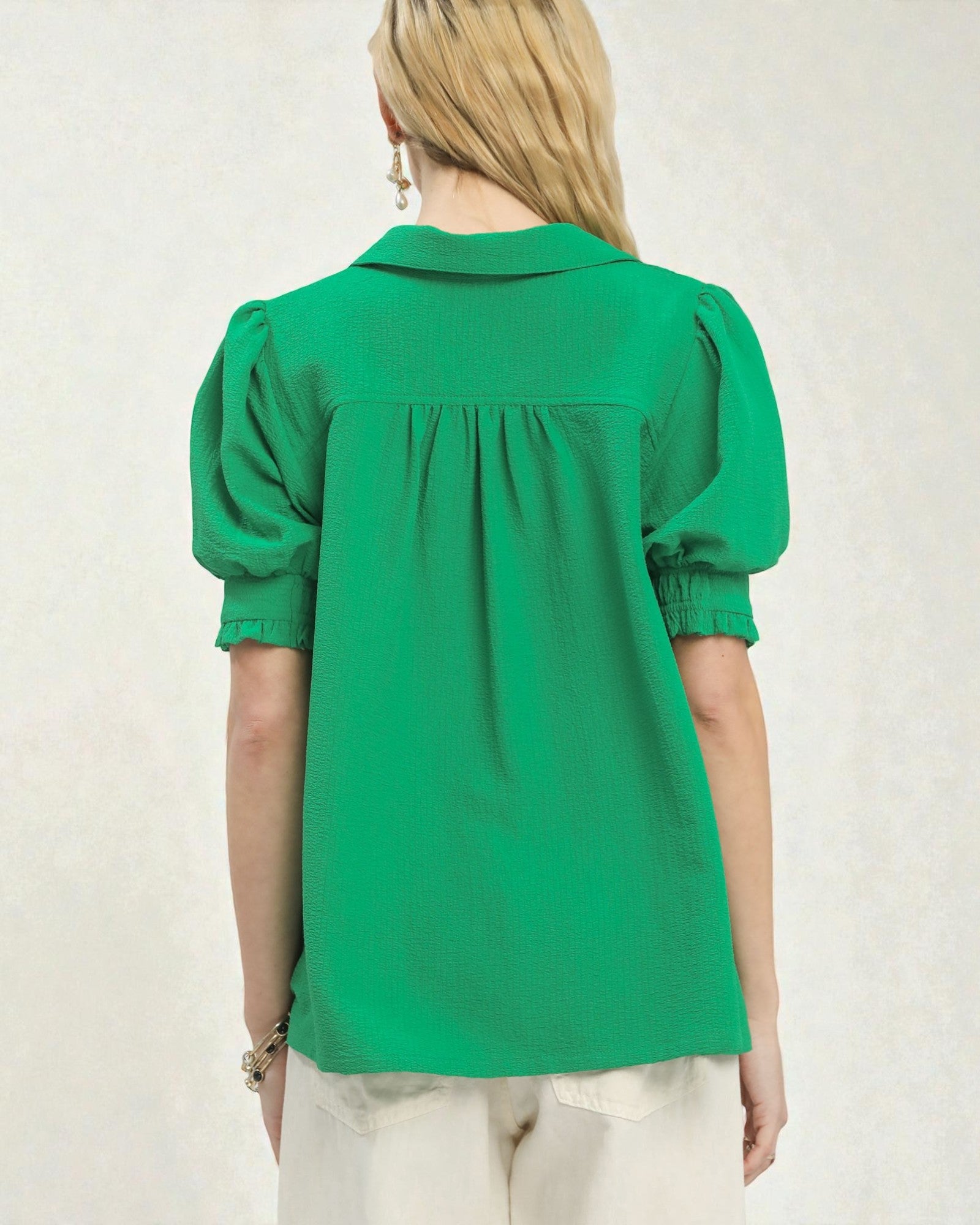 Person wearing a green blouse with puff sleeves on a plain background