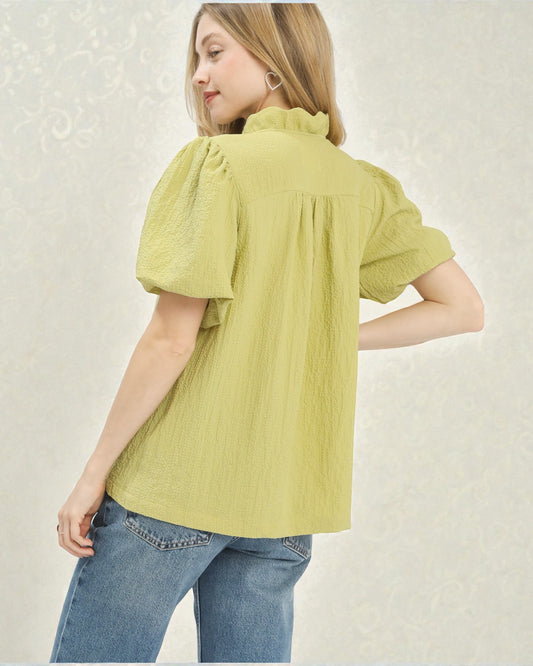 Woman wearing a green blouse with short sleeves and blue jeans on a light background