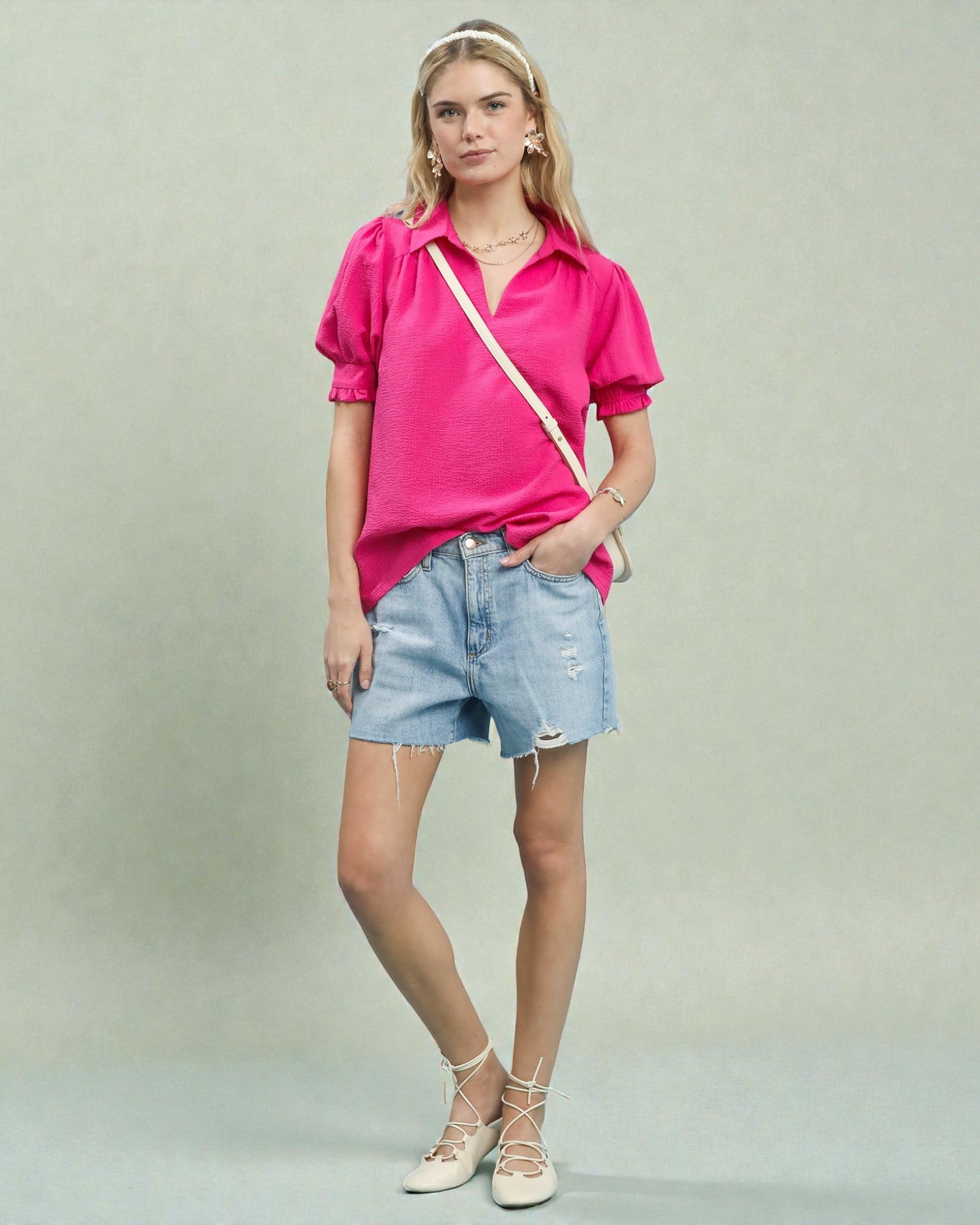 Woman wearing a pink shirt and denim shorts against a plain background