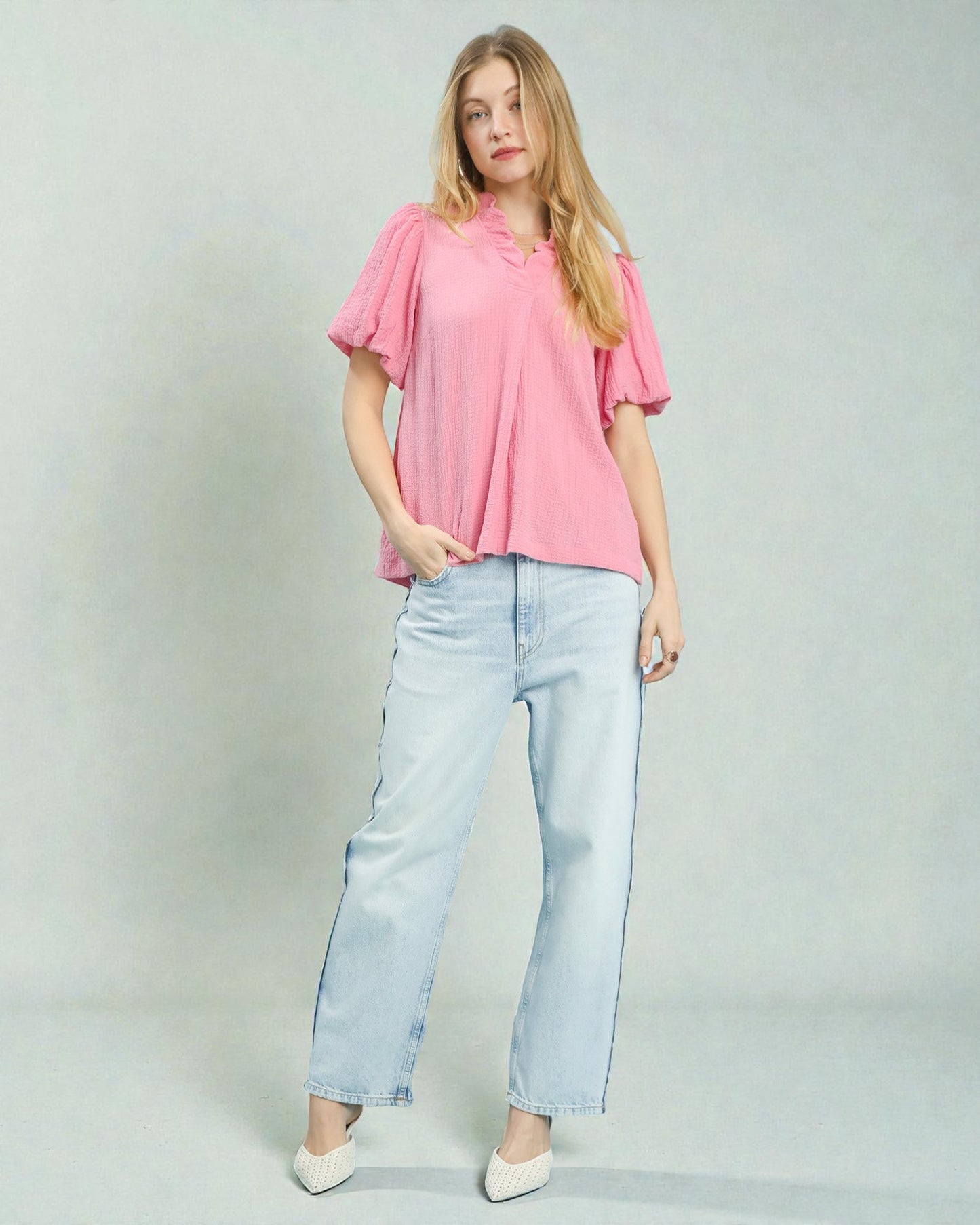 Woman wearing a pink blouse and light blue jeans on a plain background