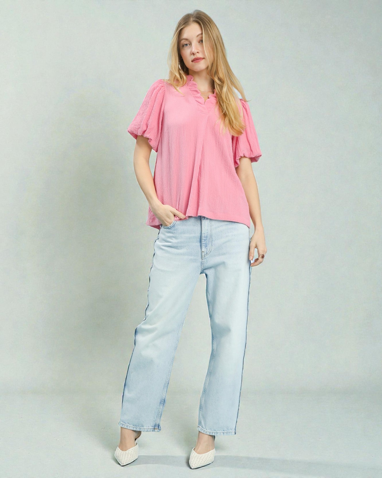Woman wearing a pink blouse and light blue jeans on a plain background