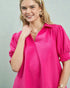 Woman wearing a bright pink blouse with puffed sleeves against a light gray background