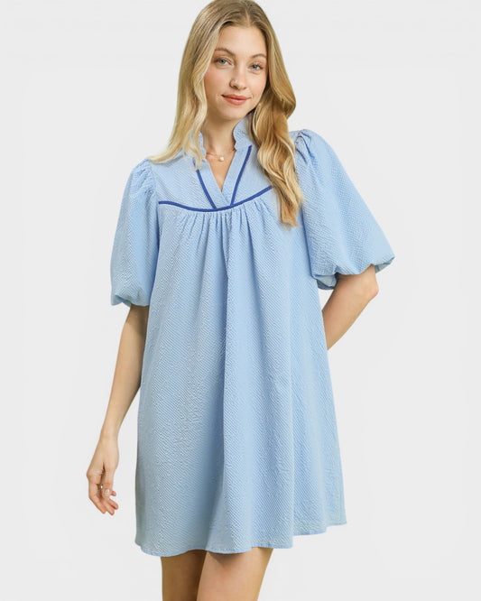 Woman wearing a light blue dress with dark blue trim on a white background