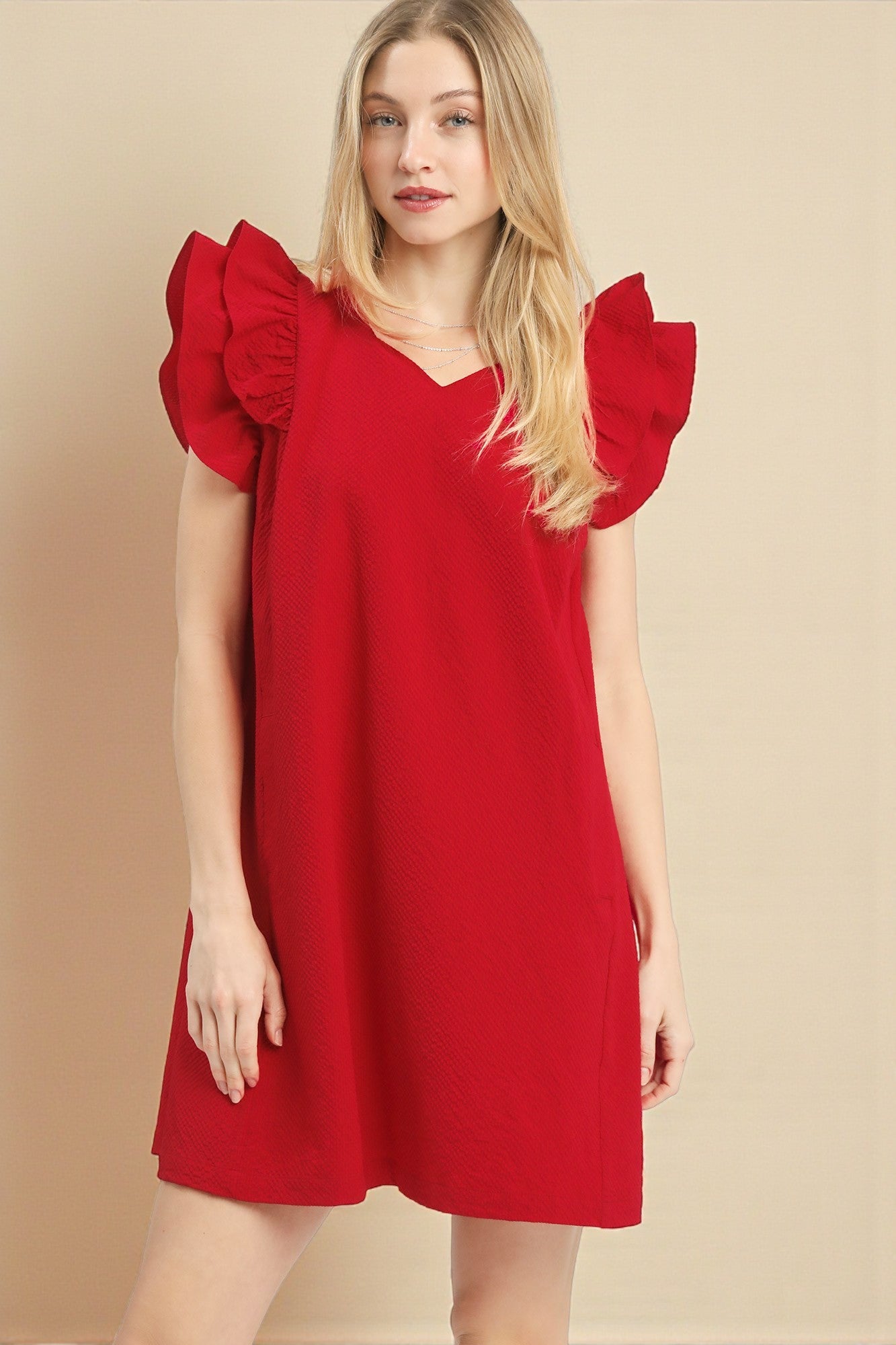 Woman wearing a red dress with ruffled sleeves on a beige background