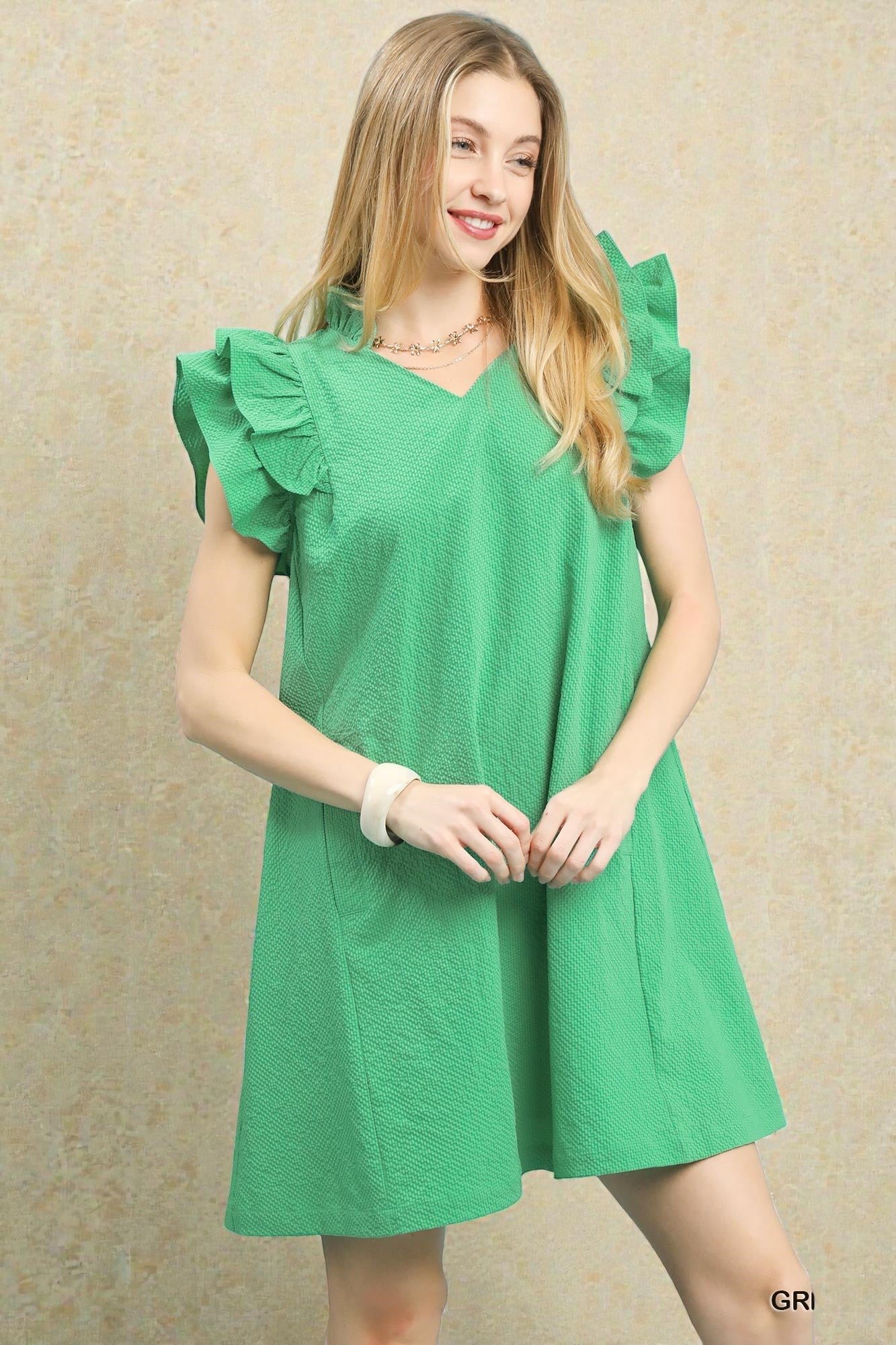 Woman wearing a green dress with ruffled sleeves against a beige background