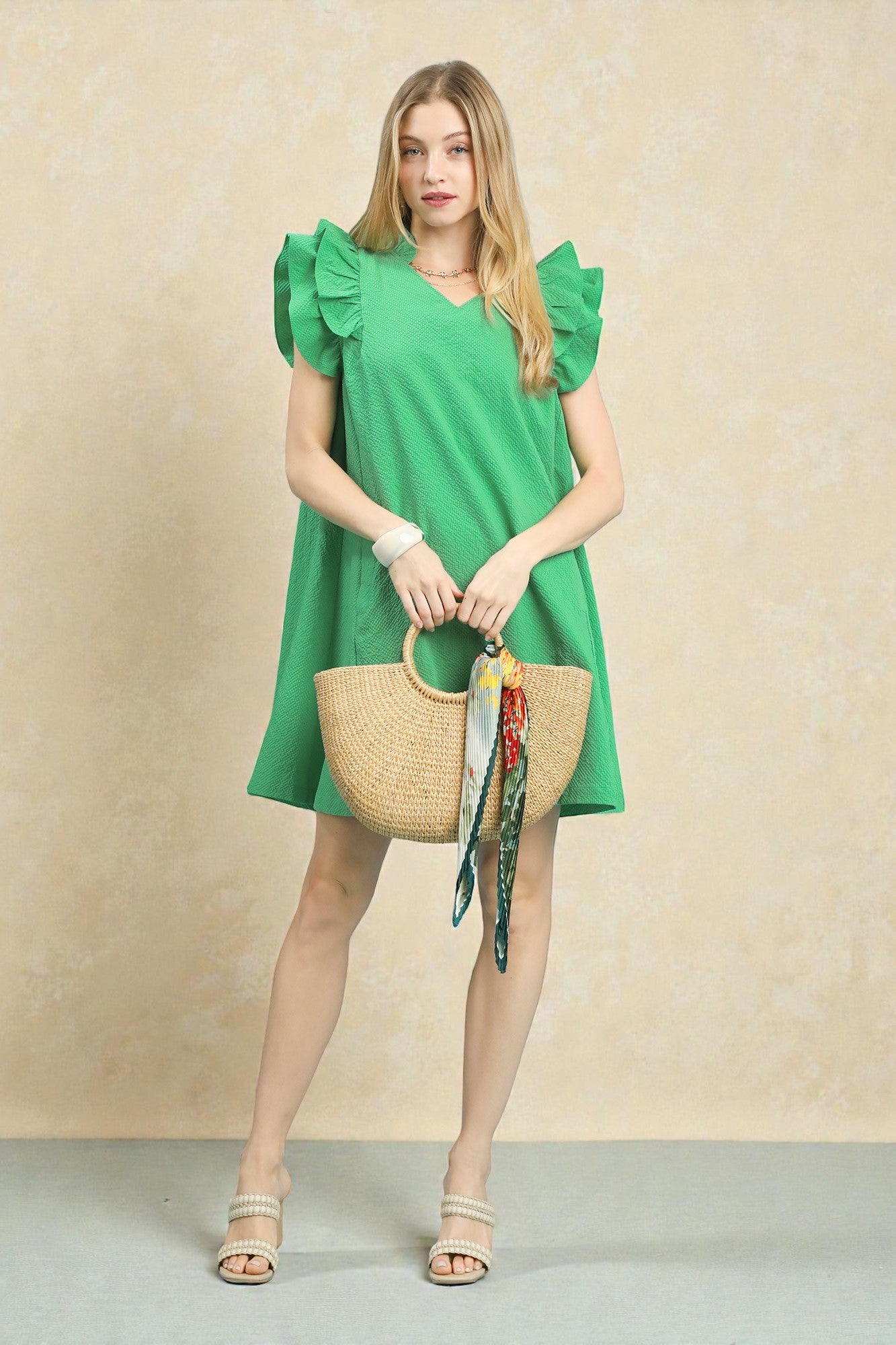 Woman in a green dress holding a straw bag against a beige background