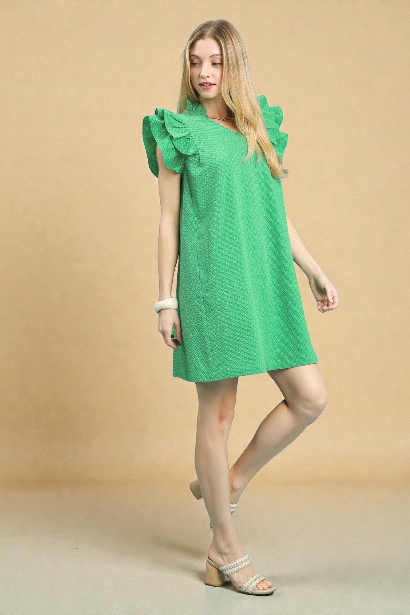 Woman wearing a green dress with ruffled sleeves against a beige background