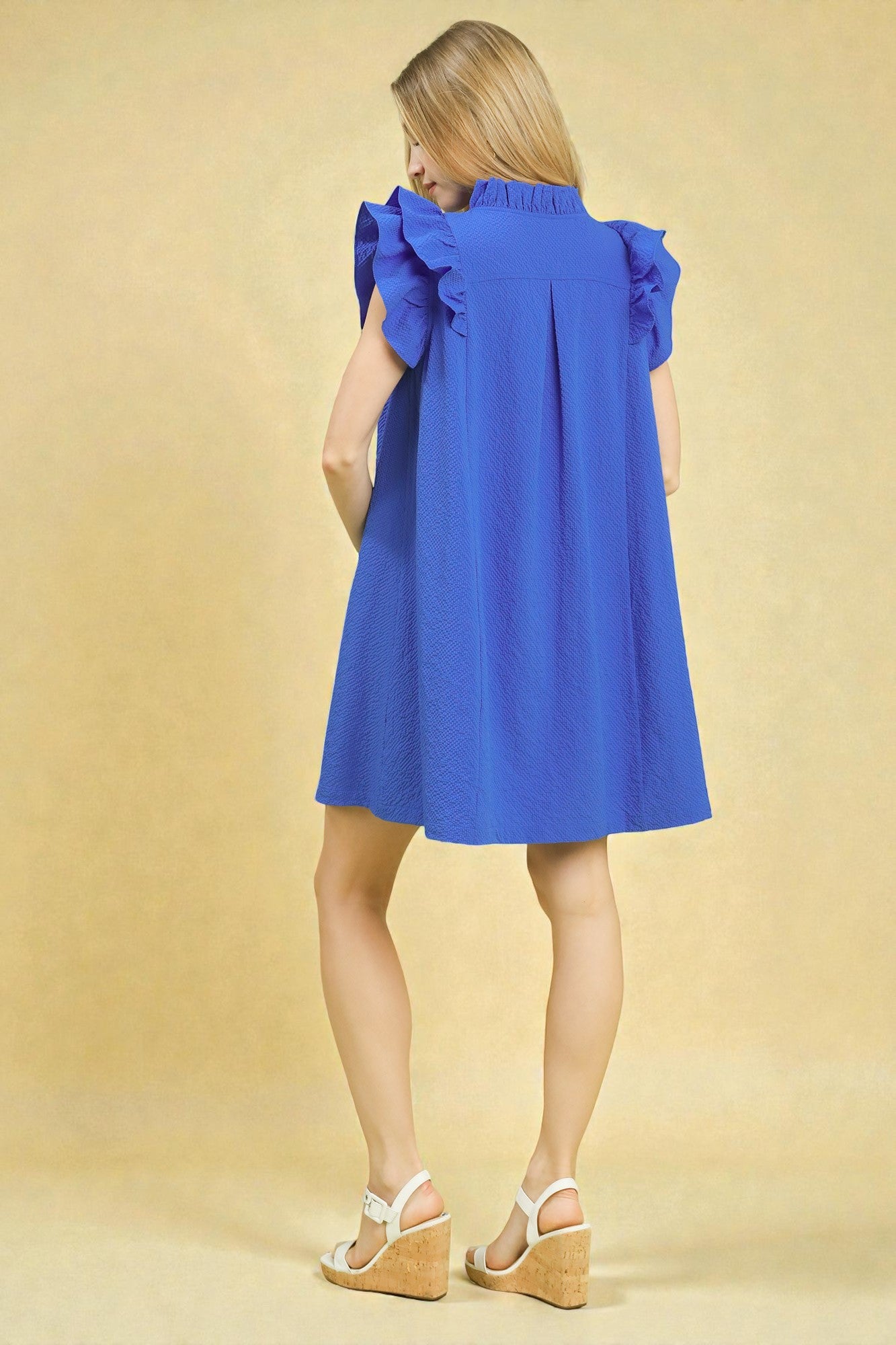 Woman wearing a blue dress with ruffled sleeves on a beige background