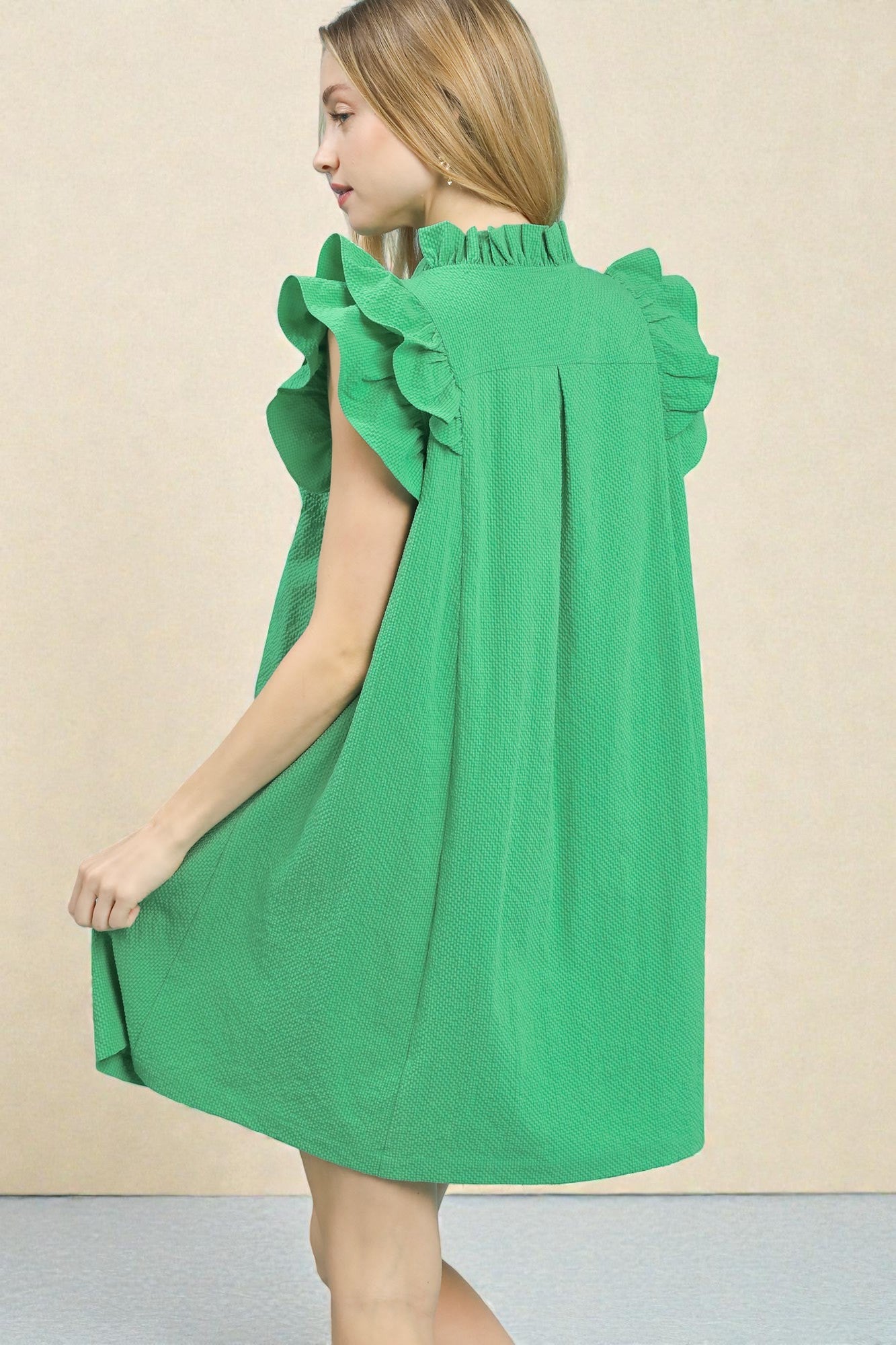 Green dress with ruffled sleeves worn by a person on a beige background