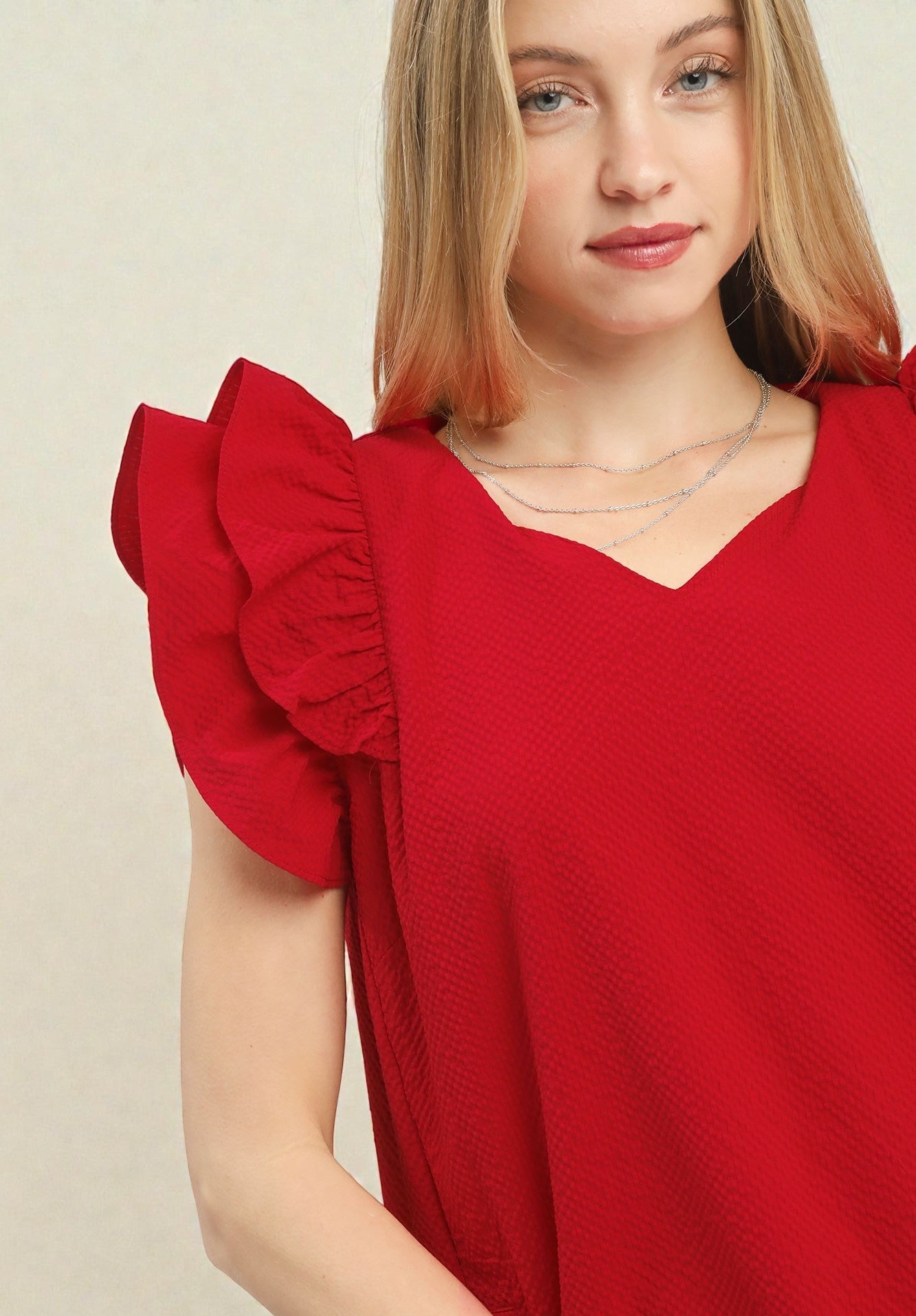 Woman wearing a red dress with ruffled sleeves against a beige background