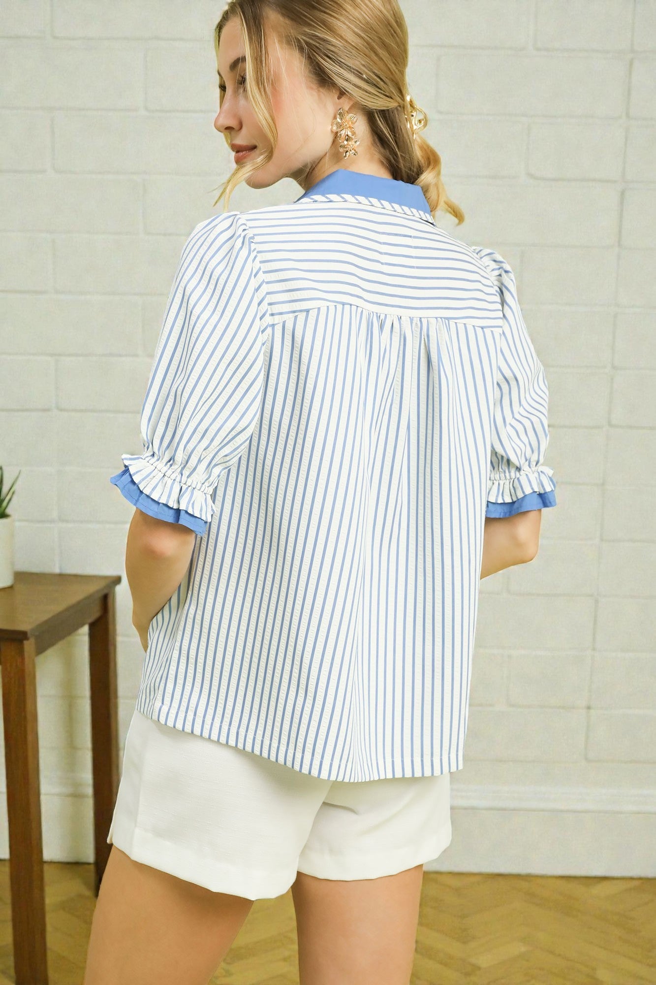 Woman wearing a blue and white striped shirt with rolled-up sleeves in a room.