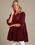 Woman wearing a burgundy sequin blouse against a beige background