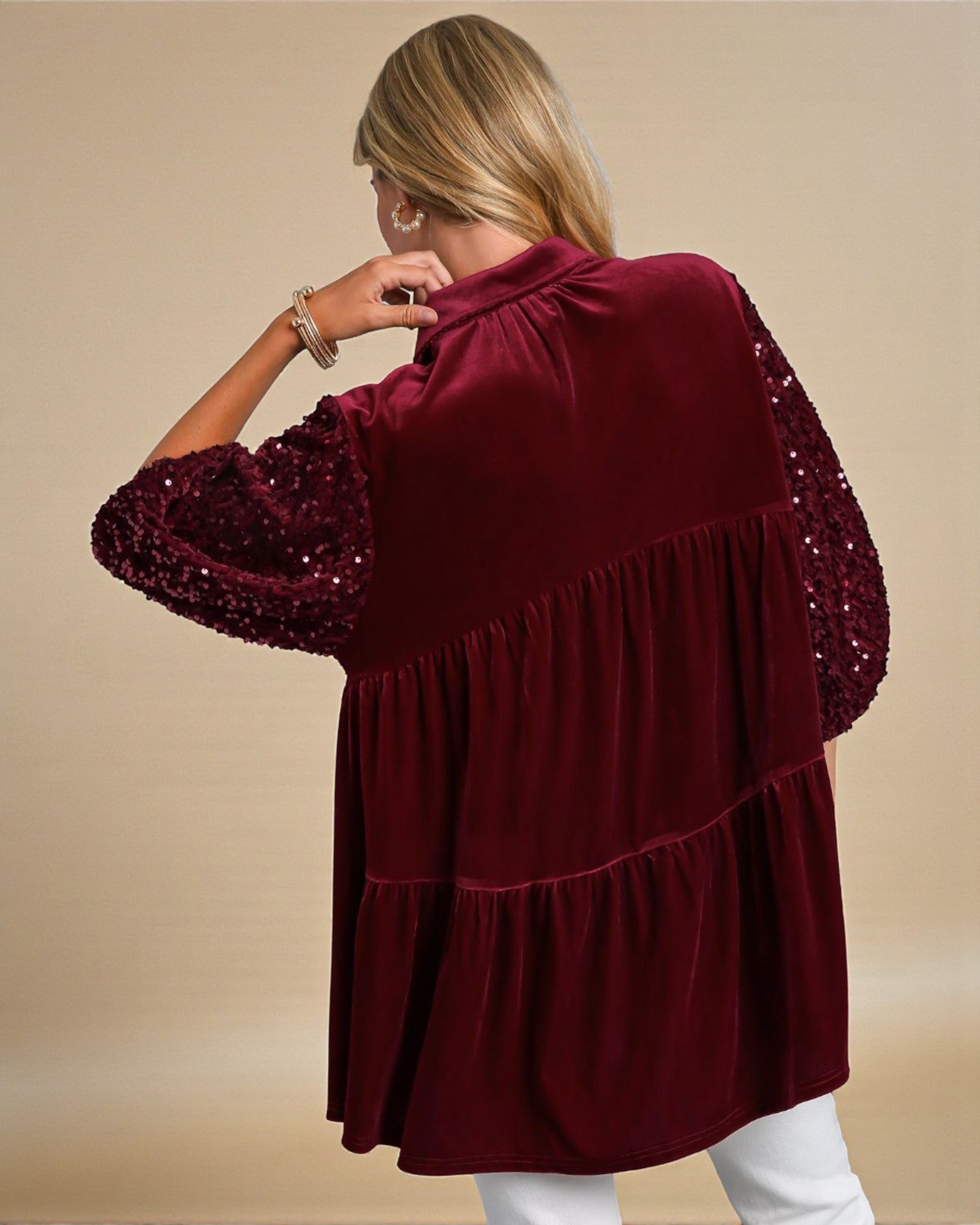 Woman wearing a burgundy velvet top with sequin sleeves on a beige background