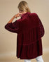 Woman wearing a burgundy velvet top with sequin sleeves on a beige background