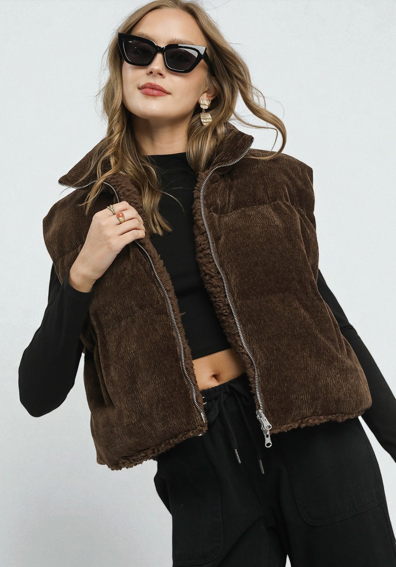 Woman wearing a brown fleece vest over a black outfit on a white background