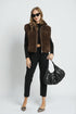 Woman wearing a brown vest, black top, and pants, holding a black handbag on a white background