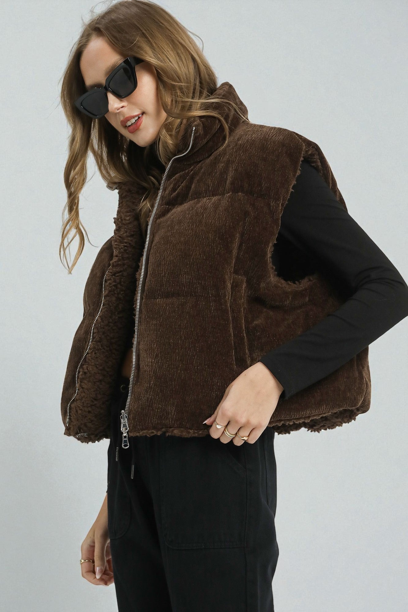 Woman wearing a brown puffer vest against a plain background
