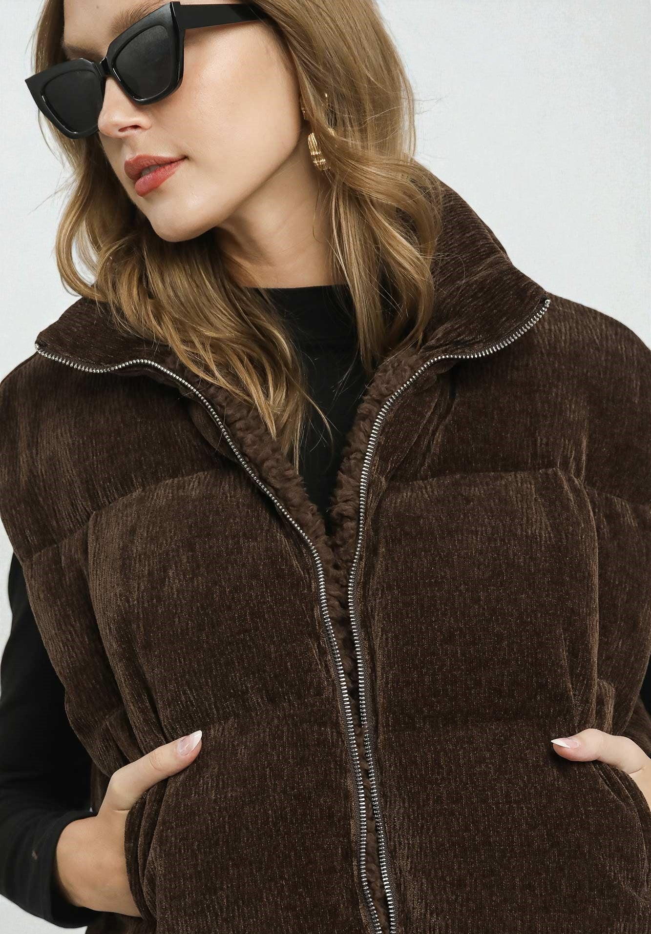 Woman wearing a brown puffer vest with a plain background