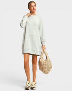 Woman wearing a light gray sweater dress holding a beige handbag on a white background