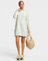 Woman wearing a light gray sweater dress holding a beige handbag on a white background