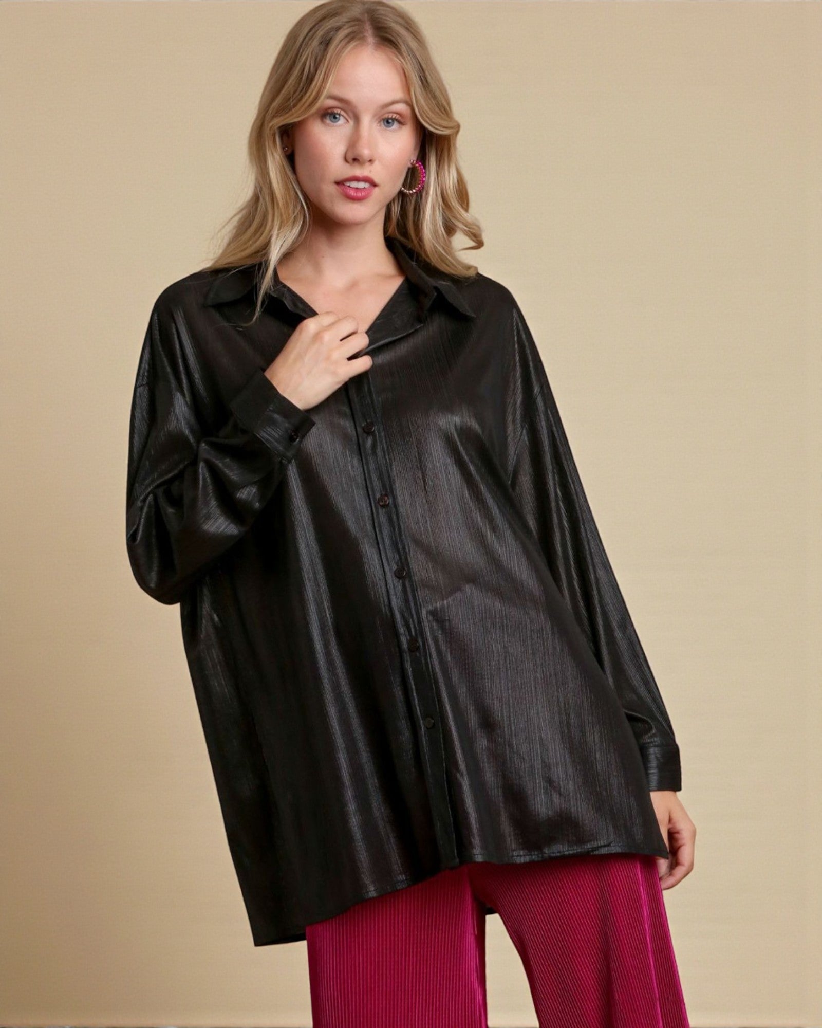Woman wearing a black satin shirt and red pants against a beige background