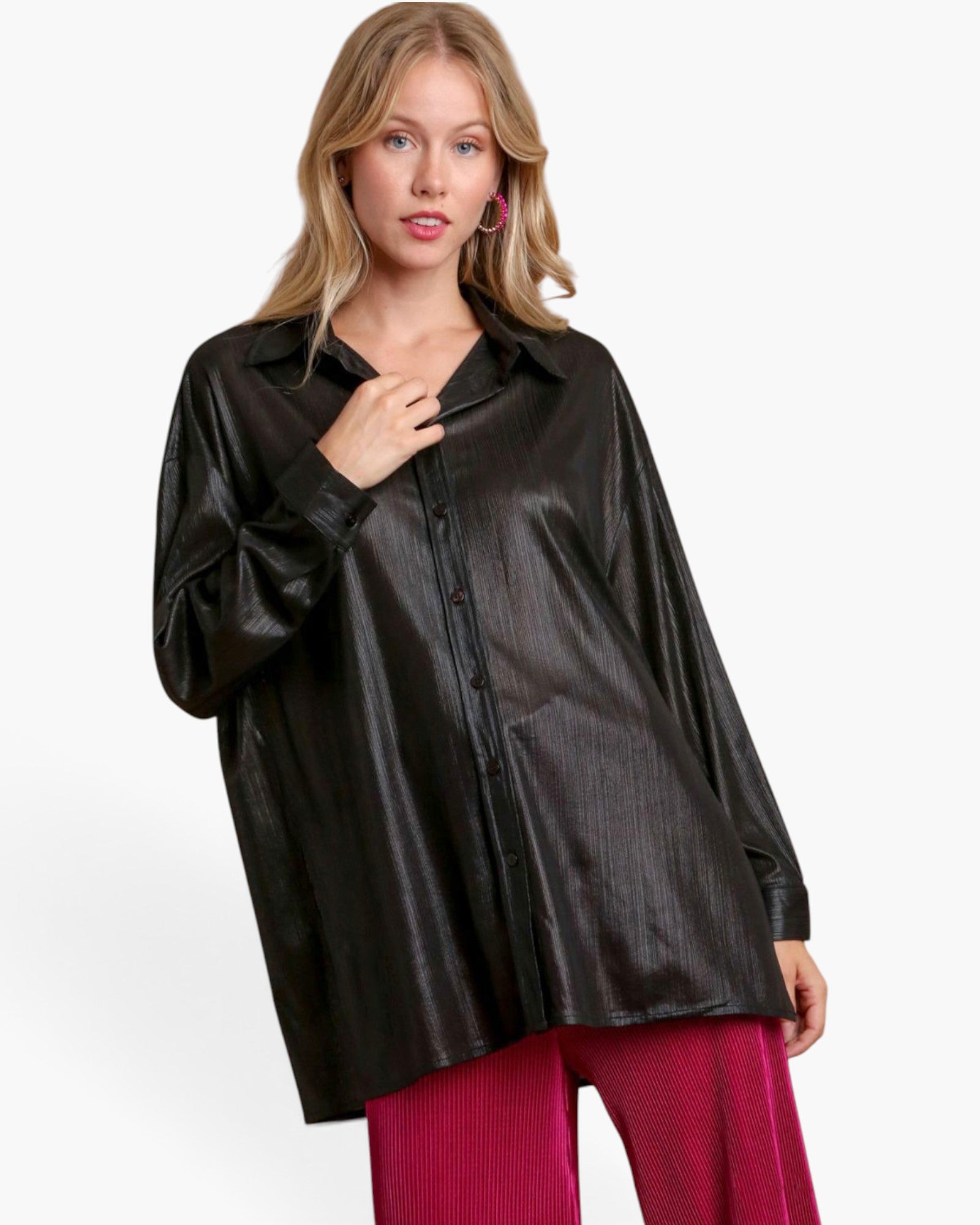 A woman modeling an oversized black faux-leather button-up shirt with a subtle vertical texture, paired with magenta ribbed pants, against a plain white studio background.