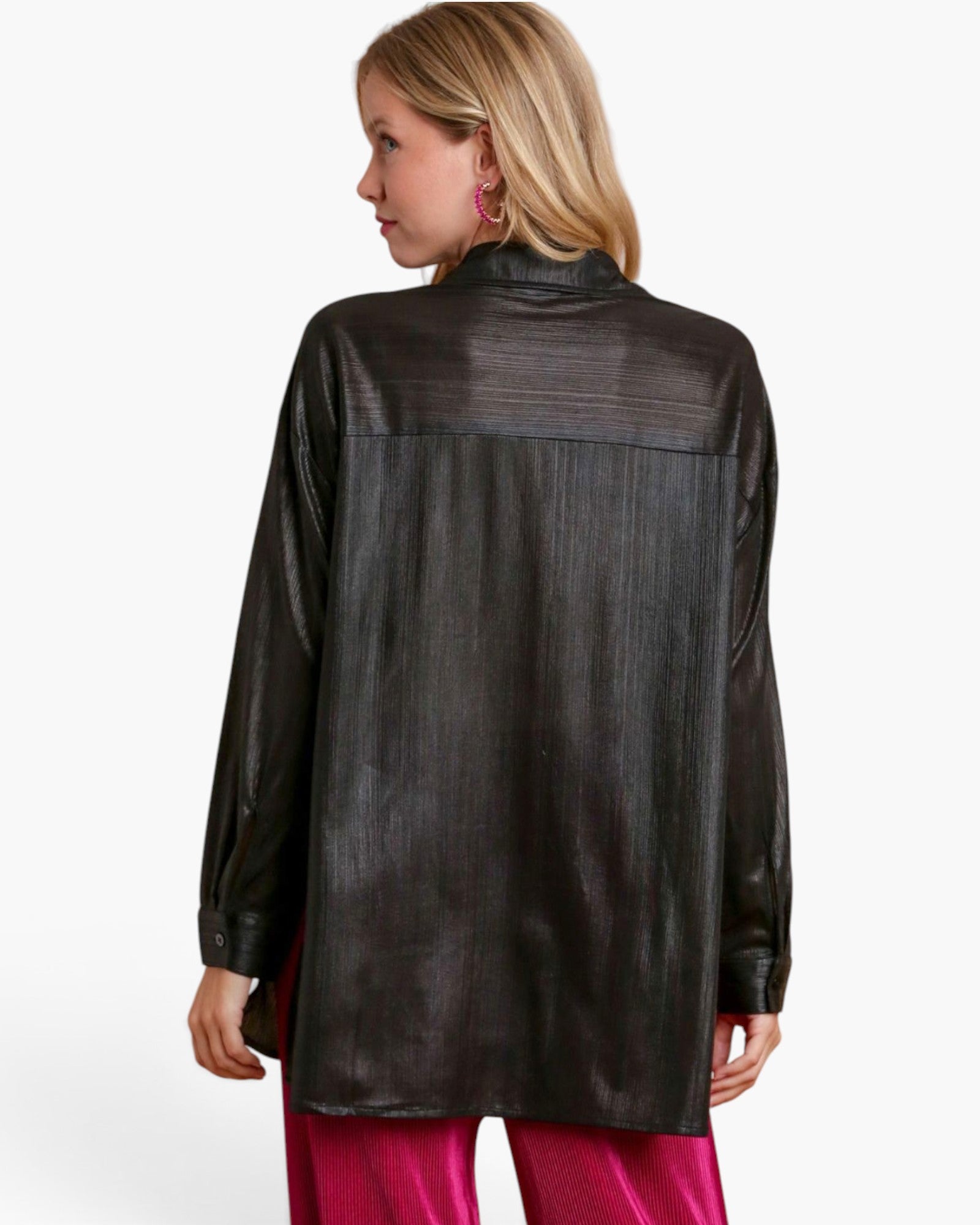 A woman shown from the back wearing a black long-sleeve textured leather or faux-leather shirt jacket with a high collar, paired with bright pink pants, against a plain white studio background.